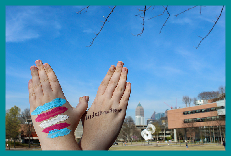 Hands forming a butterfly in front of Clough. One "wing" has the trans flag and the other one the word "Indestructible."